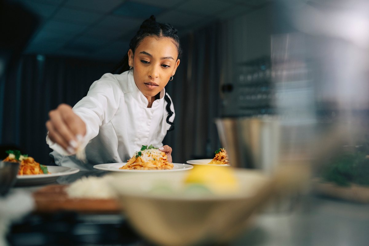 A chef sprinkles cheese over a plate of pasta